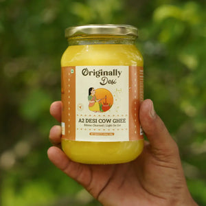 Hand holding a jar of 'Originally Desi' A2 Desi Cow Ghee with a blurred green background